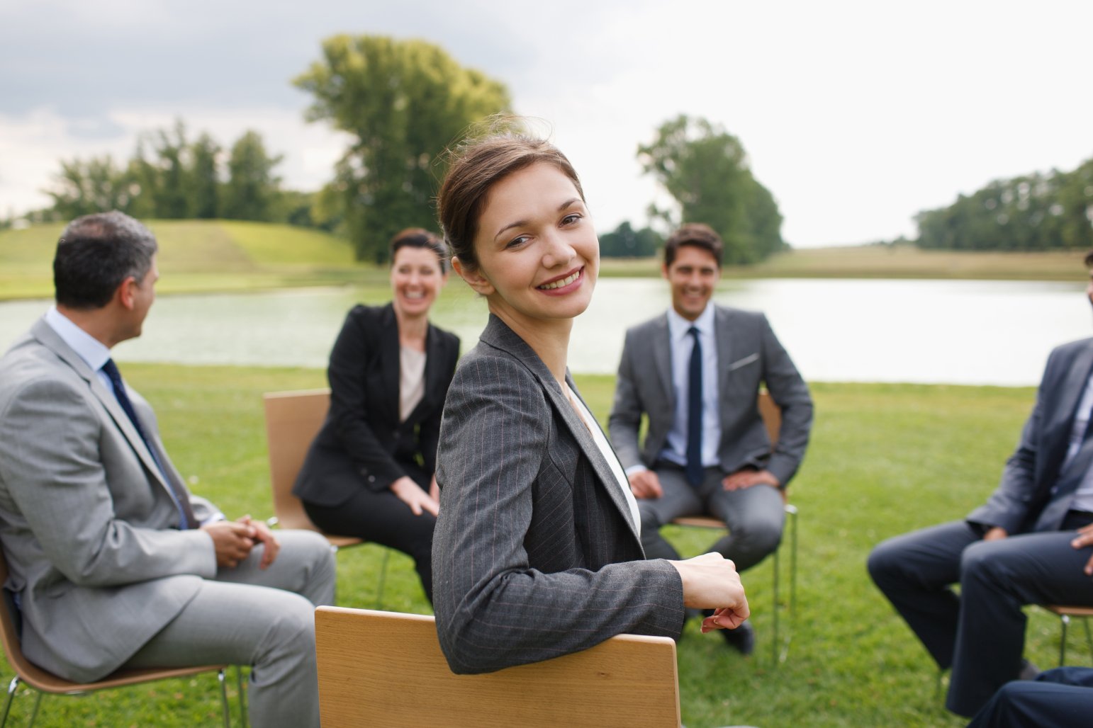 Image of five people in official costumes, sitting in a circle near a lake, all smiling and looking relaxed